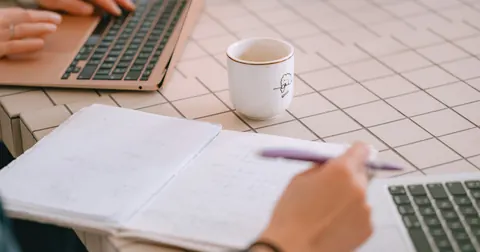 Two people working on laptops with notes and coffee